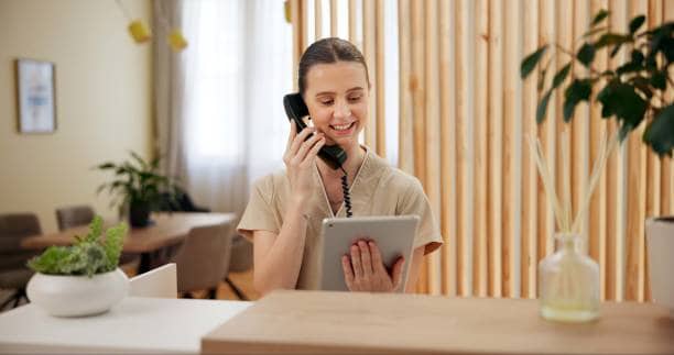 Resepsjonist svarer i telefon mens hun bruker et nettbrett